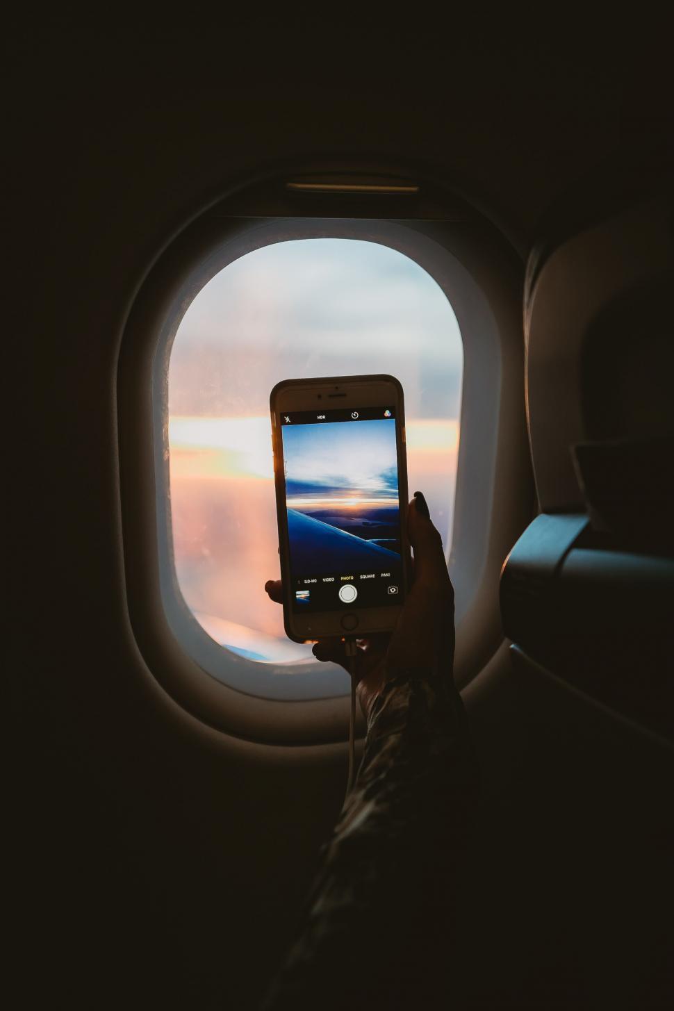 Free Image of A hand holding a phone taking a picture of a sunset through a window 