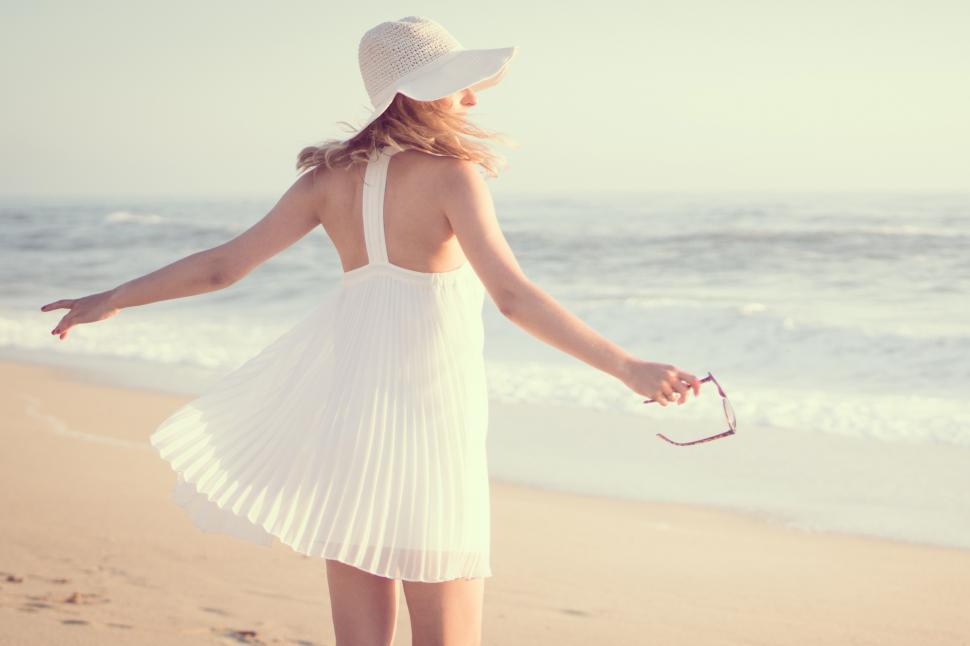 Free Image of A woman in a white dress and hat on a beach 