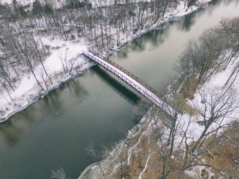 Free Image of A bridge over a river with snow covered trees 