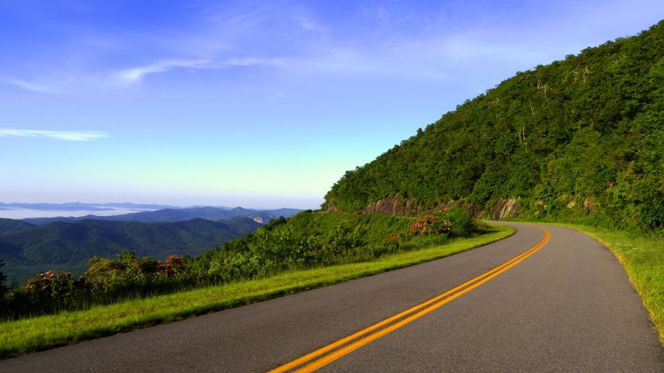 Free Image of A road with a green hill and trees 