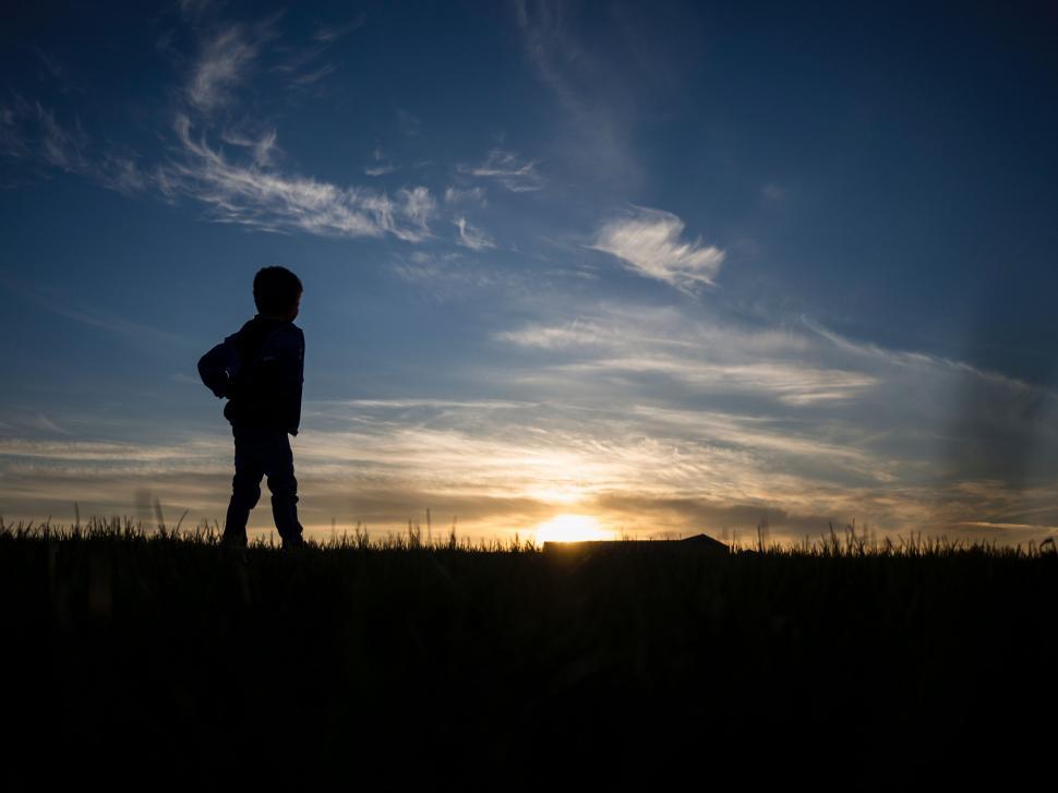 Free Image of A child standing in a field with a sunset in the background 