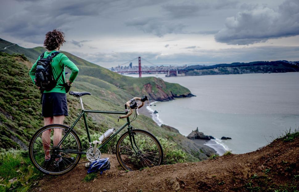 Free Image of A man standing next to a bicycle overlooking a body of water 