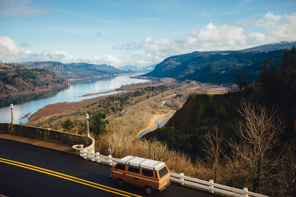Free Image of A van driving on a road with a river and mountains in the background 