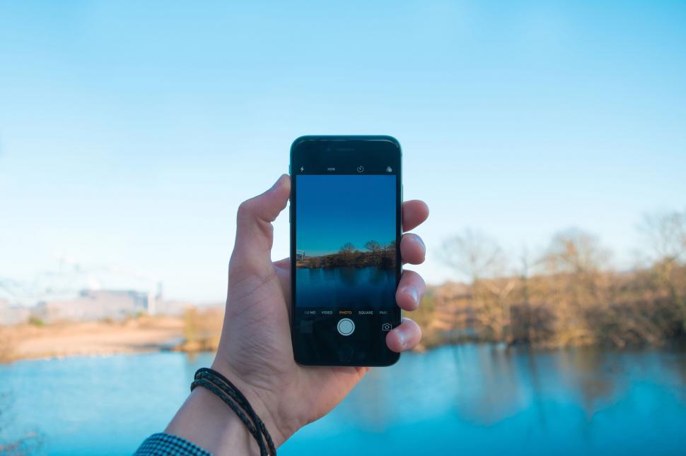 Free Image of A hand holding a phone with a lake in the background 