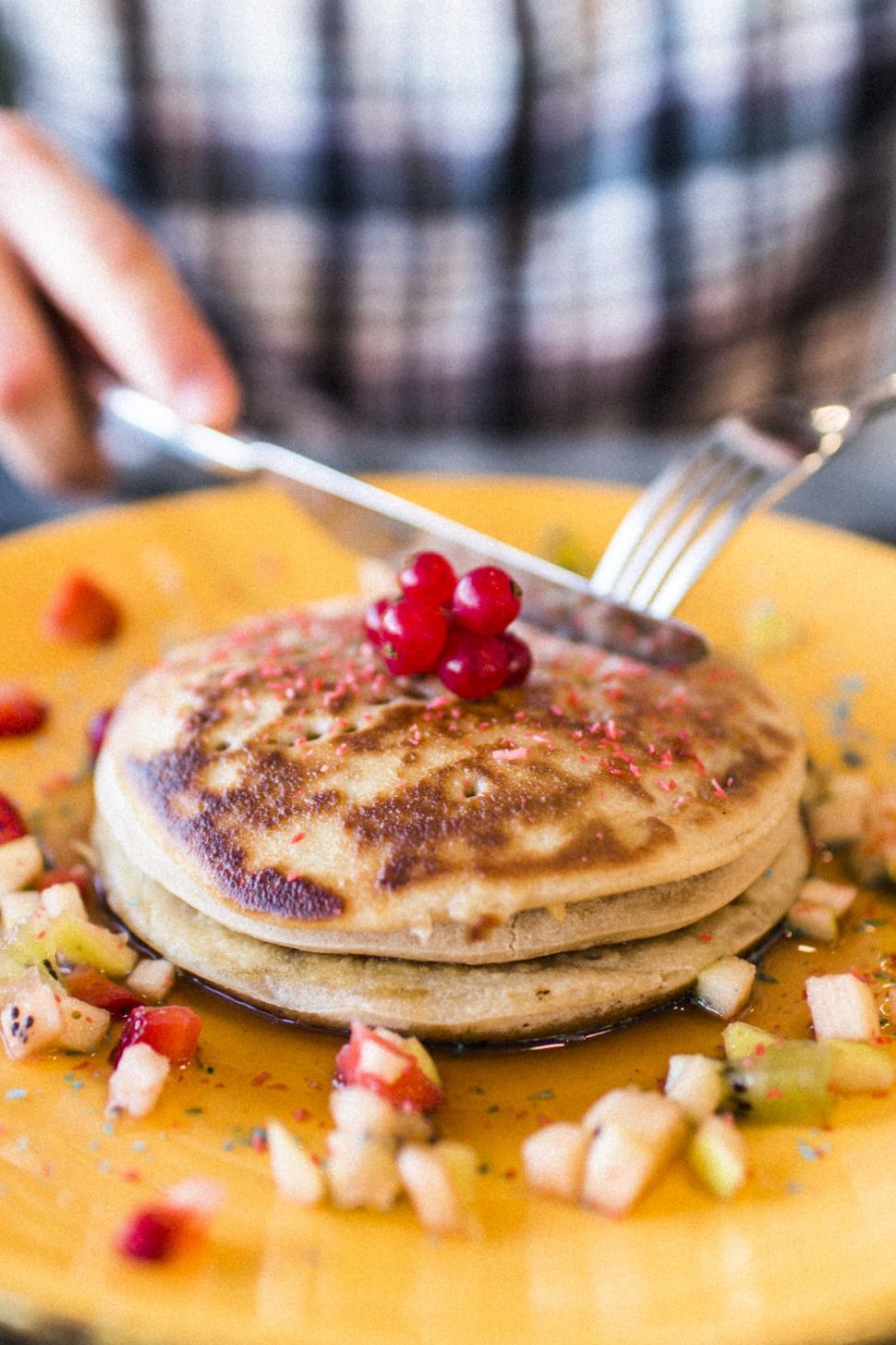 Free Image of A fork and knife cutting a stack of pancakes with fruit 