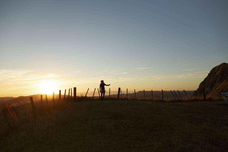 Free Image of A person standing in a field with a fence and a sunset 