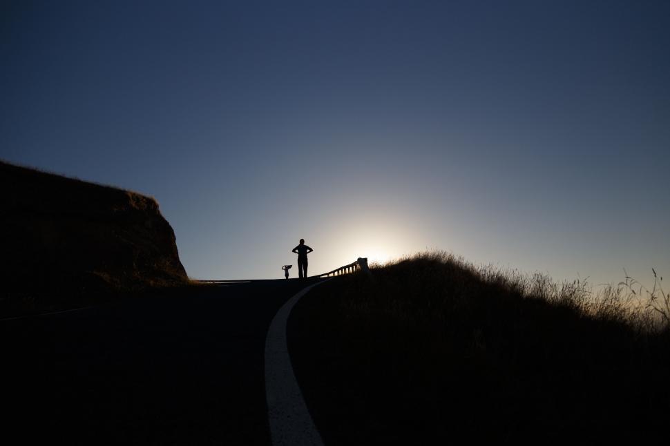 Free Image of A silhouette of a person and a dog on a road 