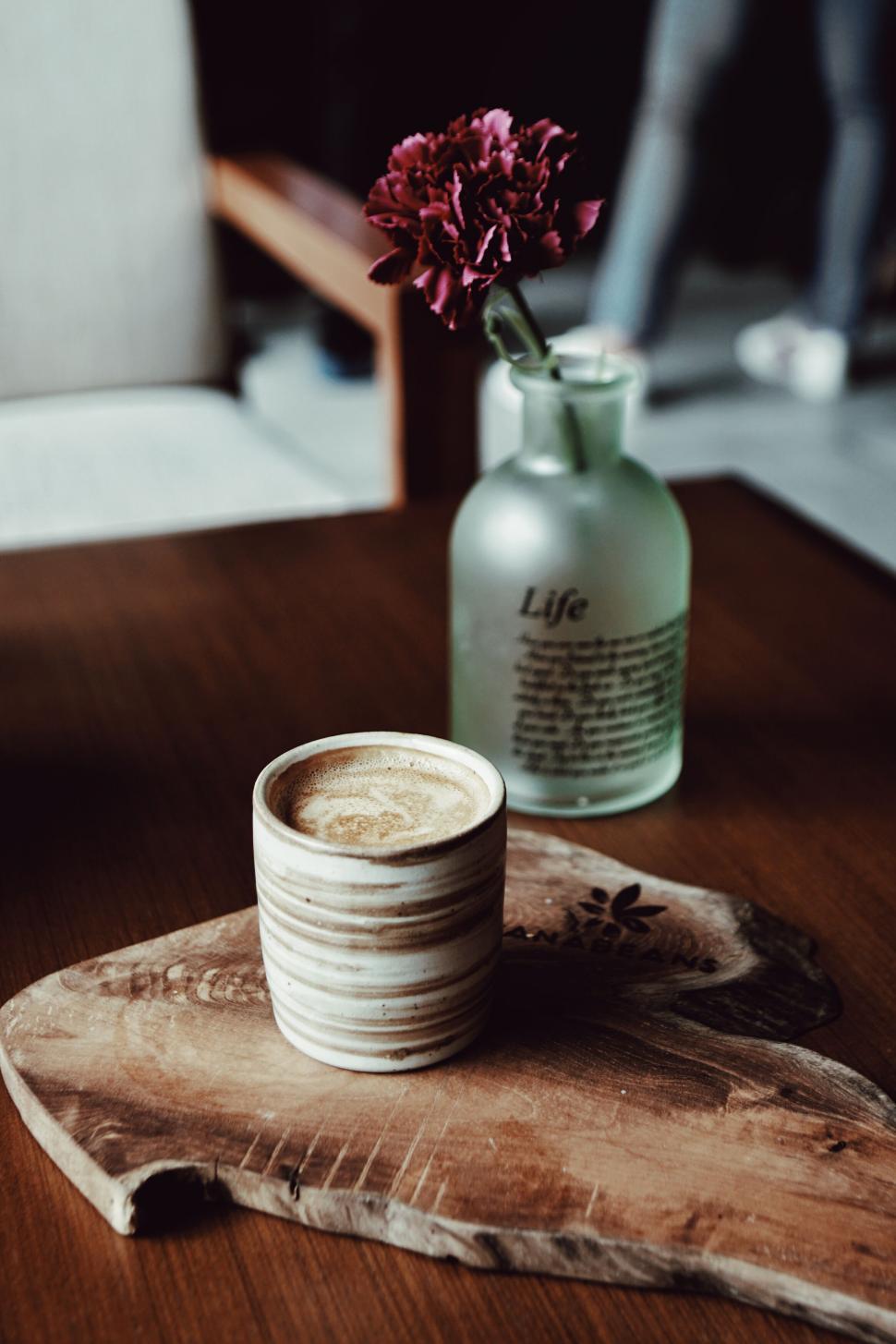 Free Image of A cup of coffee and a vase of flowers on a wood surface 
