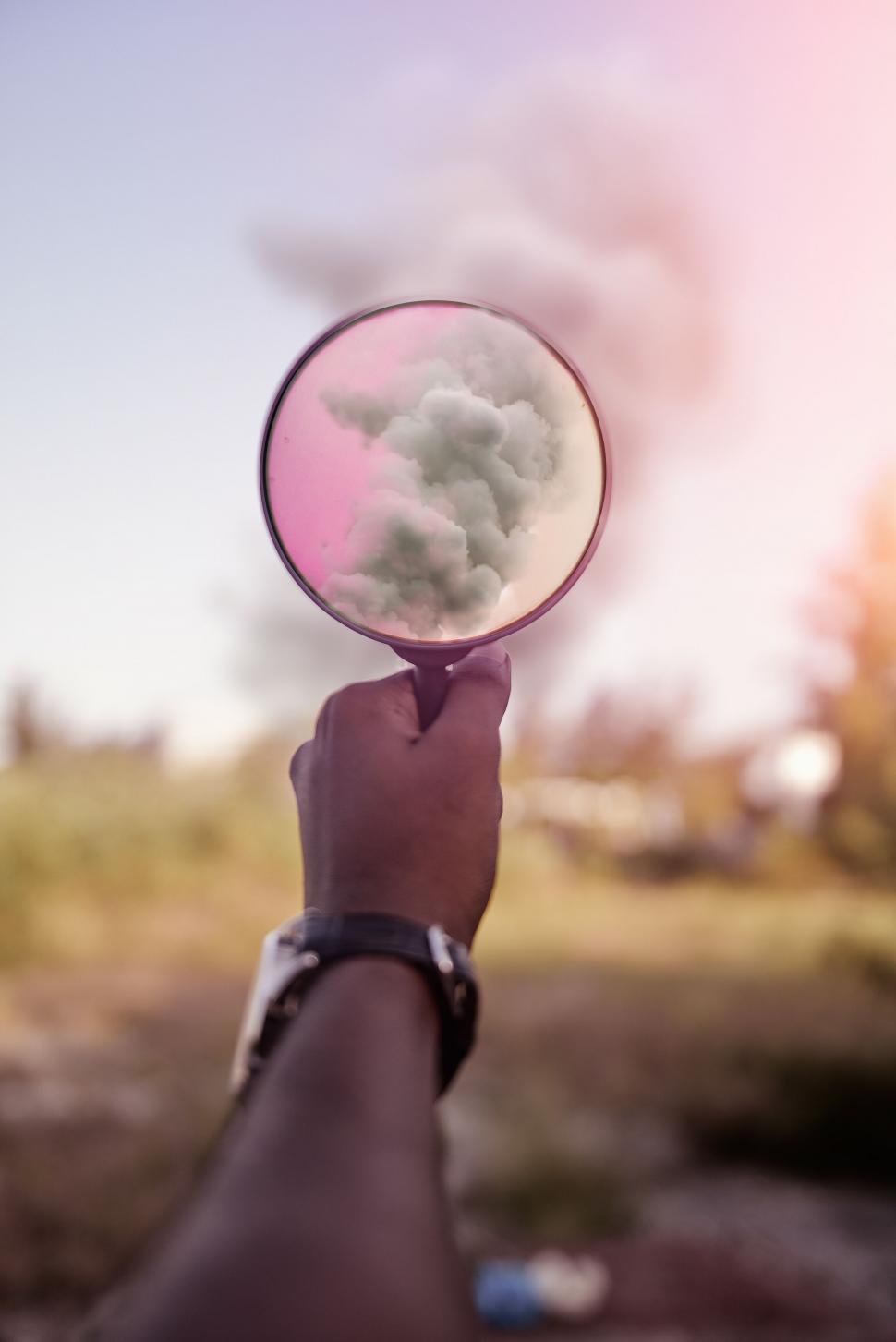 Free Image of A hand holding a magnifying glass with a pink and white cloud 