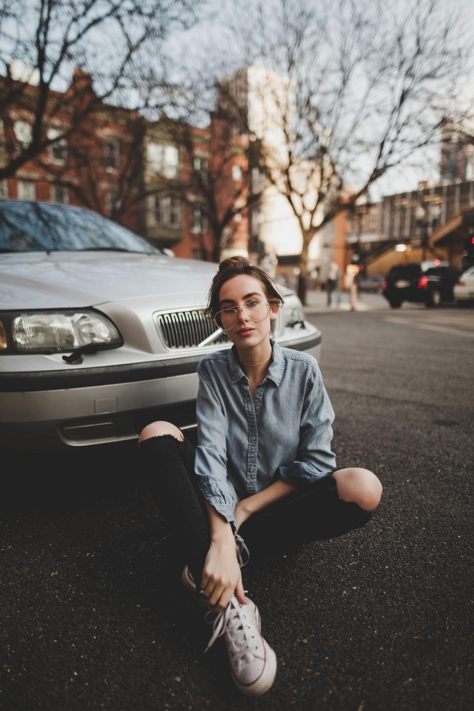 Free Image of A woman sitting on the ground in front of a car 