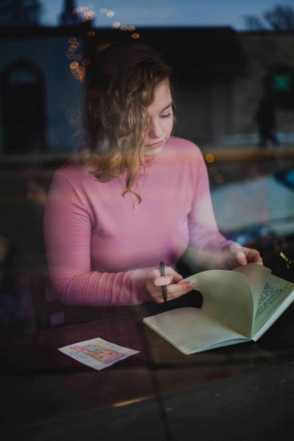 Free Image of A woman sitting at a table writing in a book 