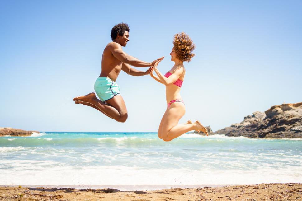 Free Image of Happy diverse couple jumping near sea 