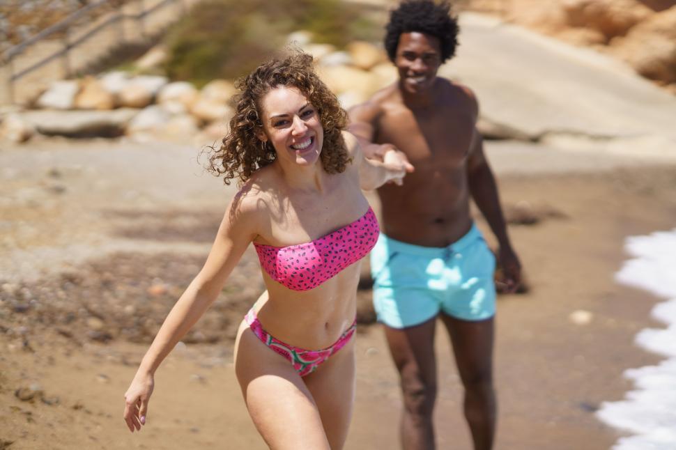 Free Image of Cheerful diverse couple holding hands while running on beach 