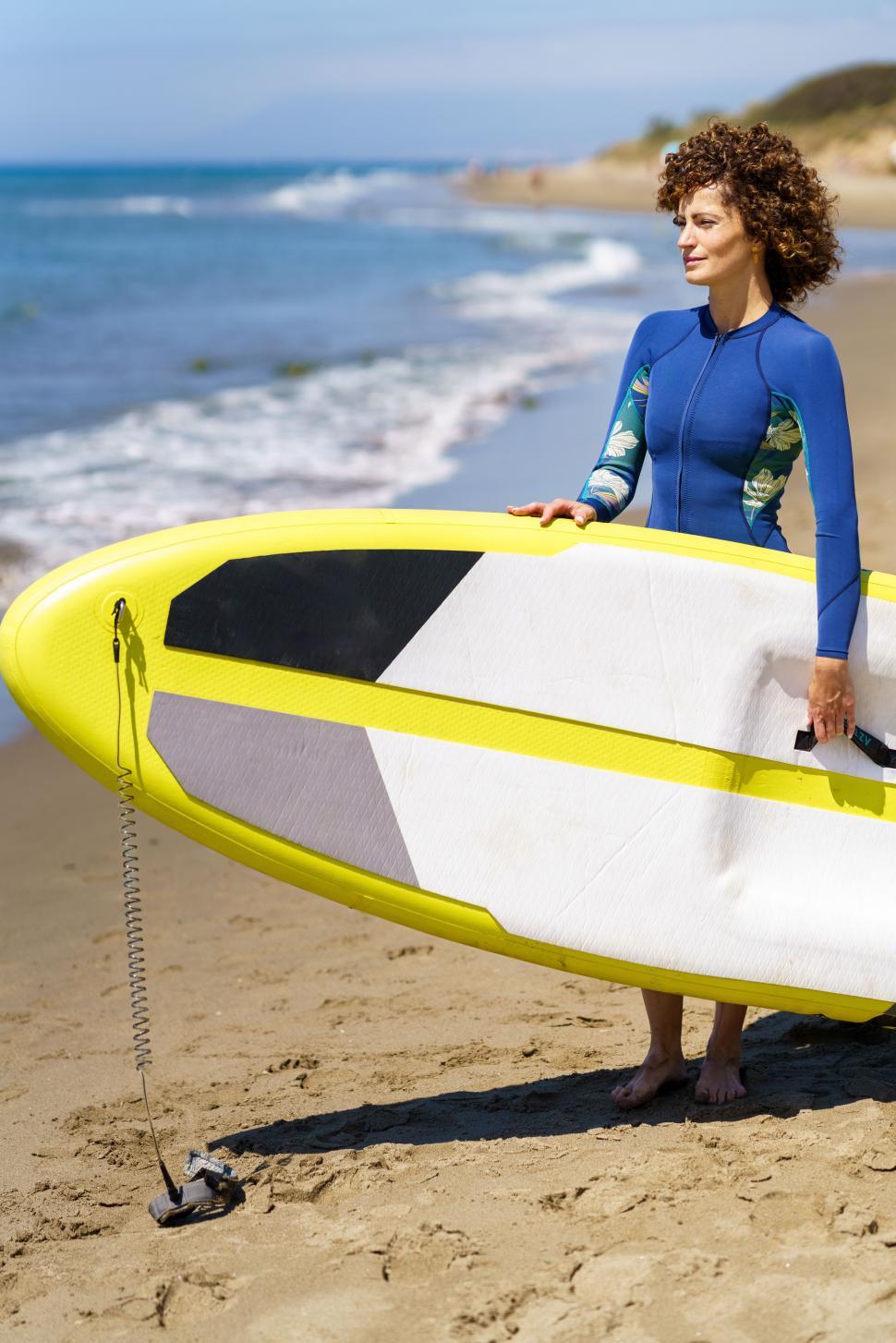 Free Image of Young woman standing with SUP board on sandy beach 