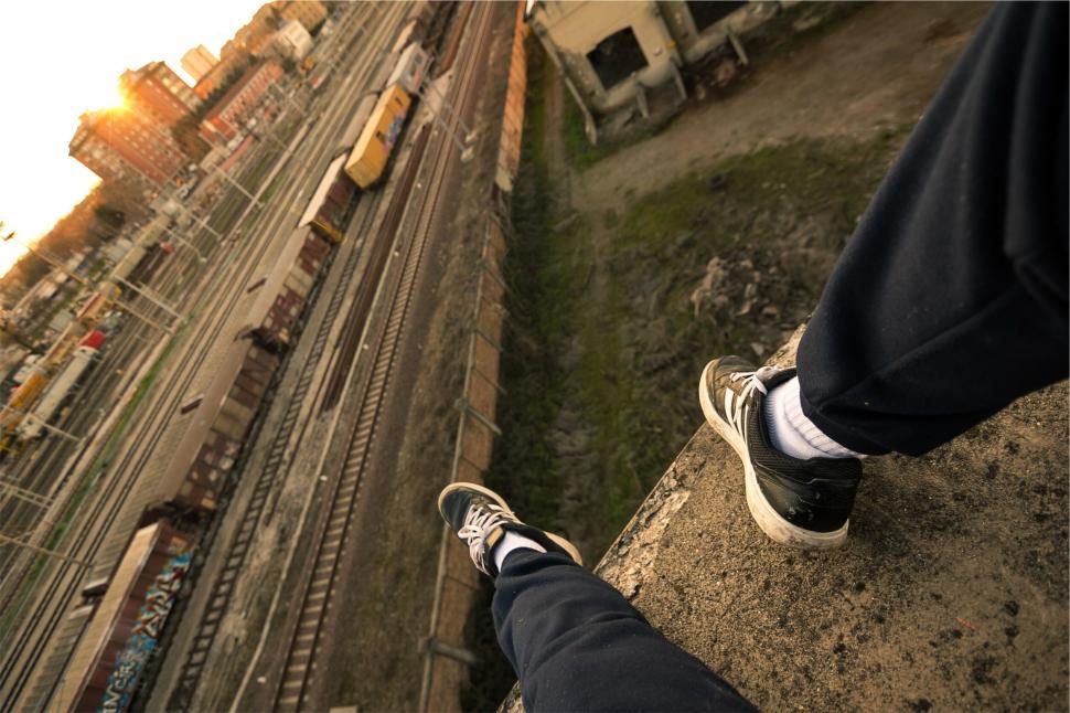 Free Image of A person s legs and feet on a ledge overlooking a city 