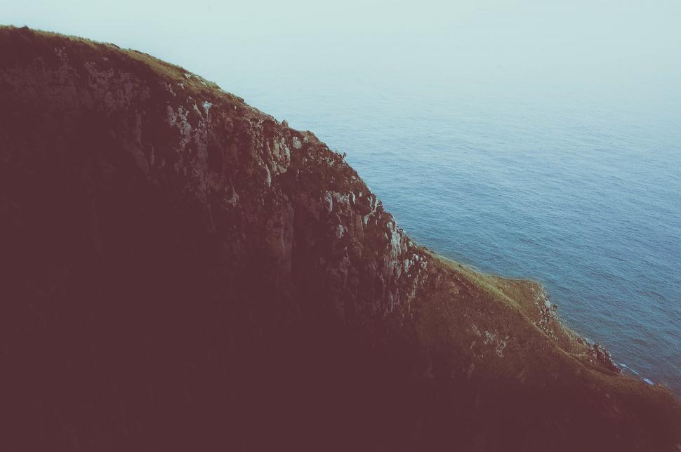 Free Image of A cliff edge with water in the background 