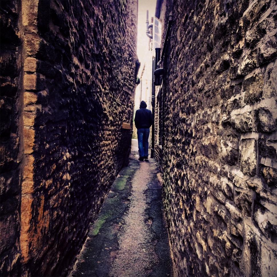 Free Image of A person walking down a narrow alley between stone buildings 