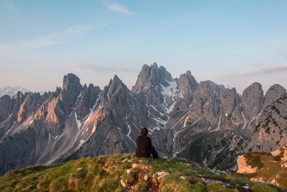 Free Image of A person sitting on a hill looking at a mountain range 