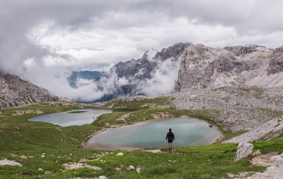 Free Image of A man standing in a grassy area with a lake in front of mountains 