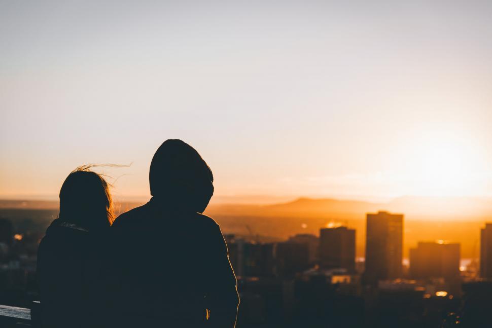 Free Image of A silhouette of a couple of people looking at a city during sunset 