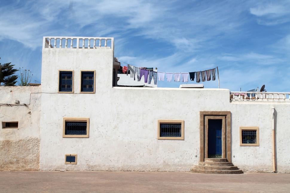 Free Image of A white building with blue door and laundry from a rope 