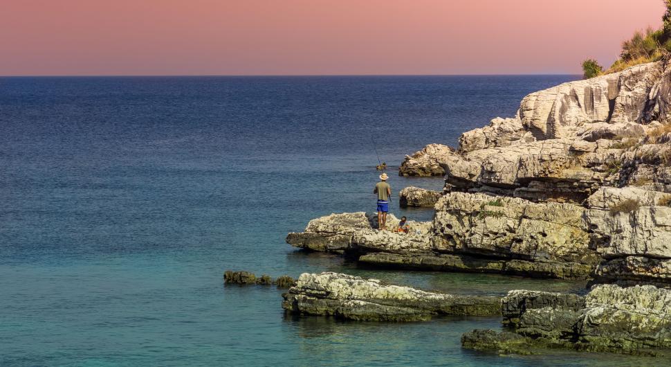 Free Image of A man standing on a rocky cliff overlooking the ocean 