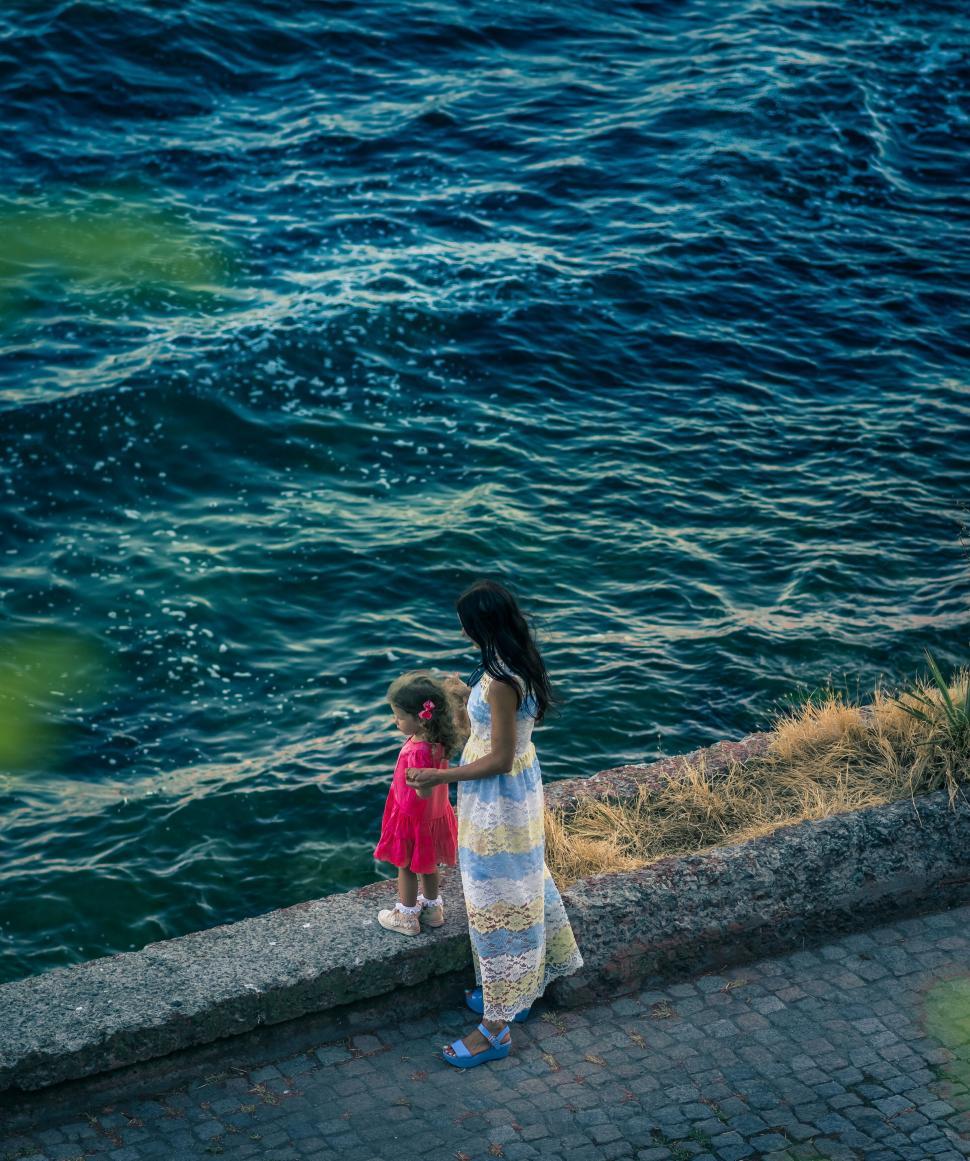 Free Image of A woman and child standing on a ledge by water 