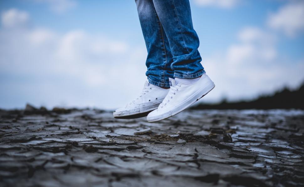Free Image of A person s legs in white shoes and jeans jumping on a cracked ground 