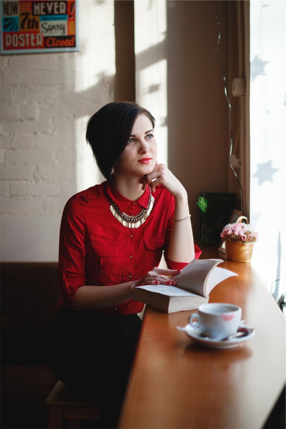 Free Image of A woman sitting at a table with a book and a cup of coffee 
