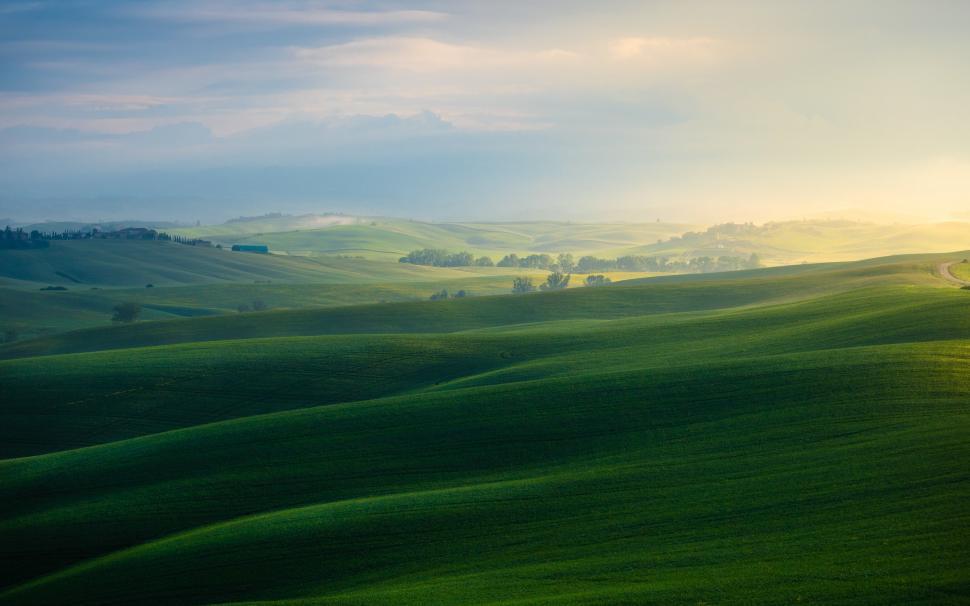 Free Image of A rolling green hills with trees and clouds 