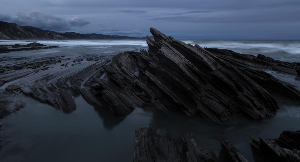 Free Image of A rocky beach with water and mountains in the background 