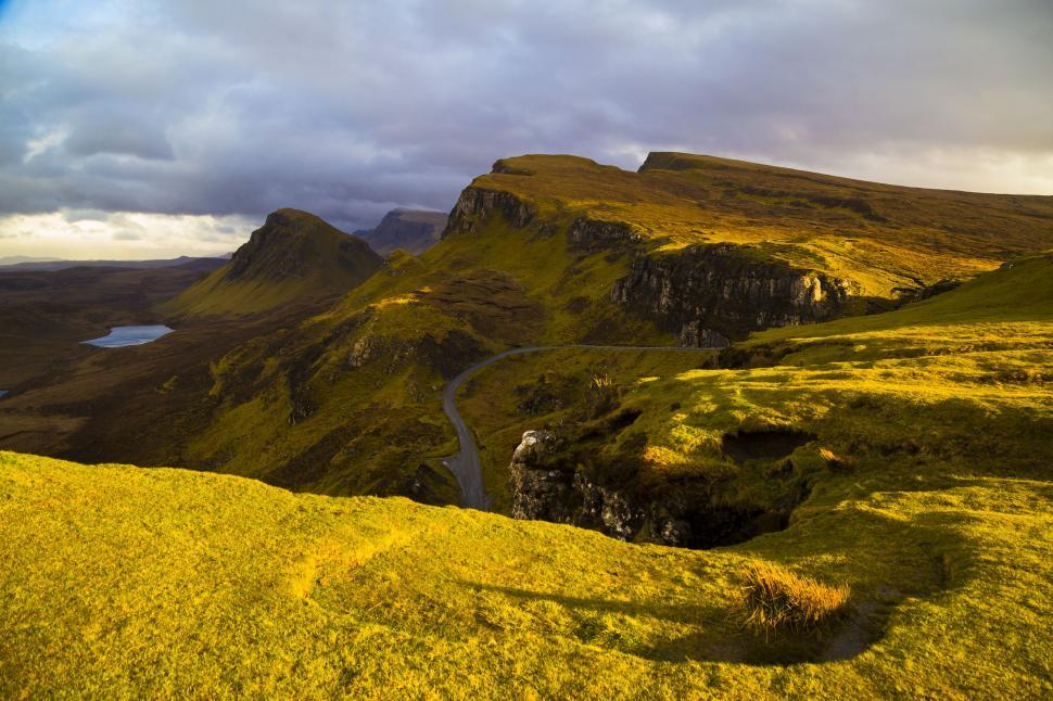 Free Image of A green hills with a road with quiraing in the background 