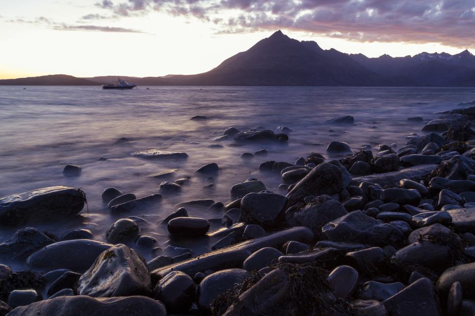Free Image of A rocky beach with a boat in the distance 