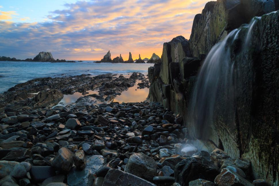 Free Image of A rocky beach with a waterfall 