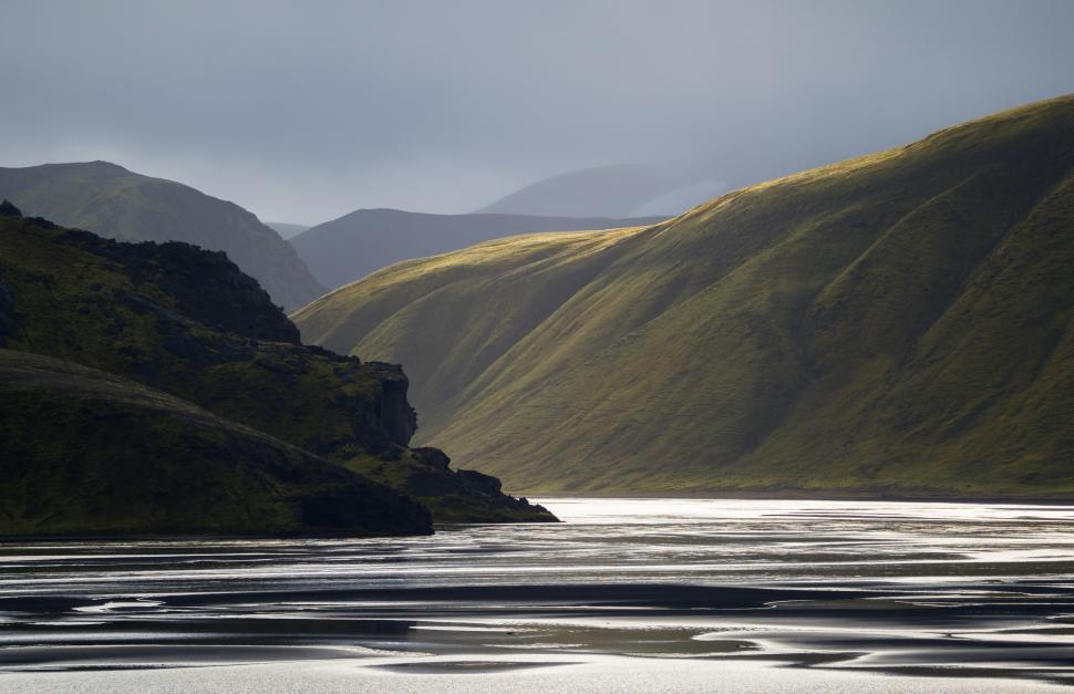 Free Image of A body of water with hills and a cloudy sky 