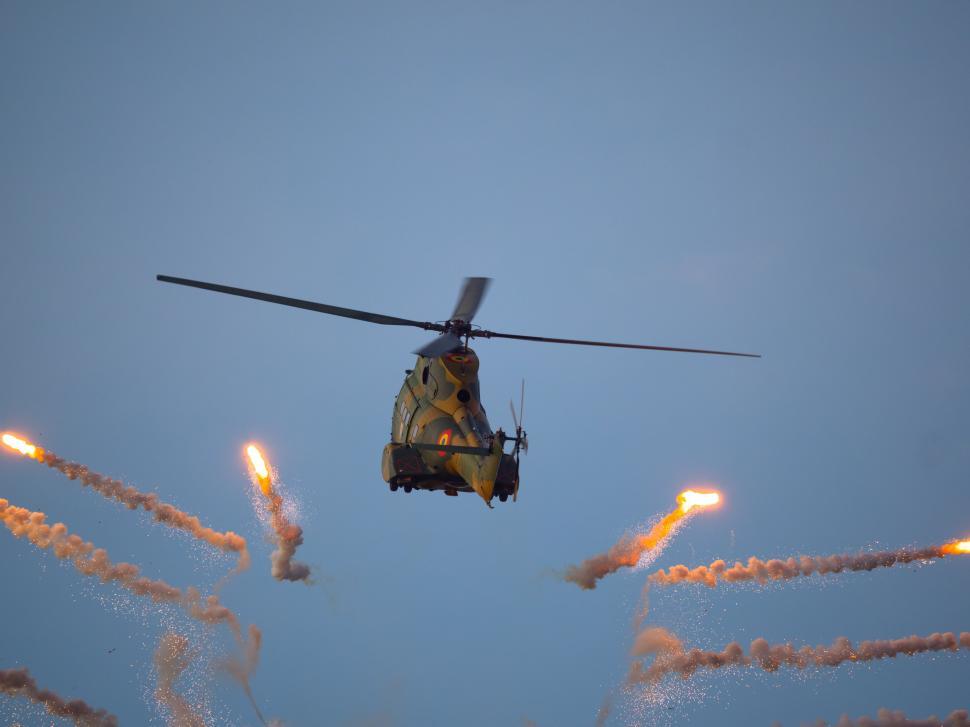 Free Image of A helicopter flying in the sky with explosions 