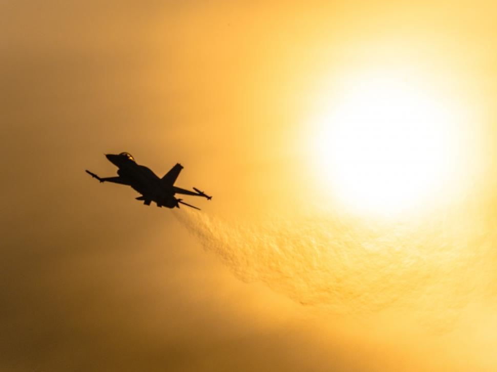 Free Image of A jet flying in the sky with the sun behind it 