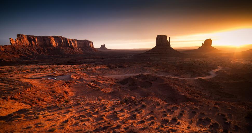 Free Image of A desert landscape with a dirt road and a large rock formation 