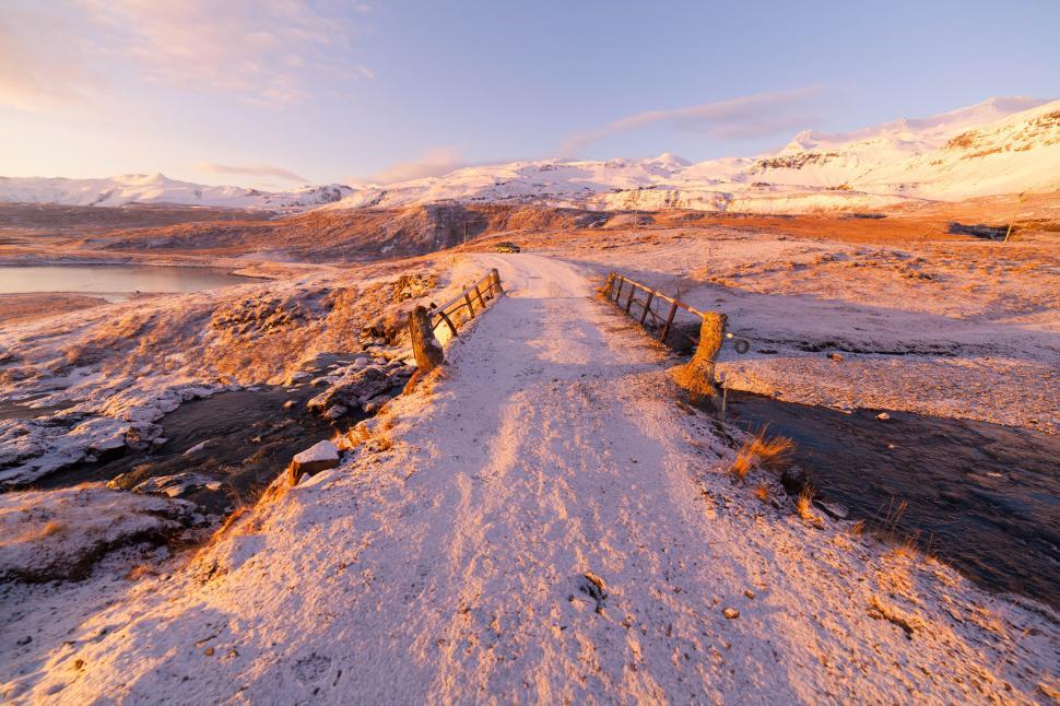 Free Image of A snowy road with a fence and a body of water in the distance 