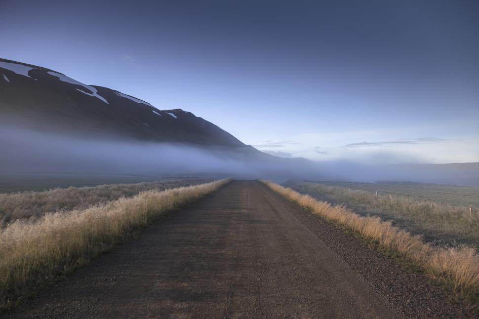 Free Image of A long dirt road with grass and mountains in the background 