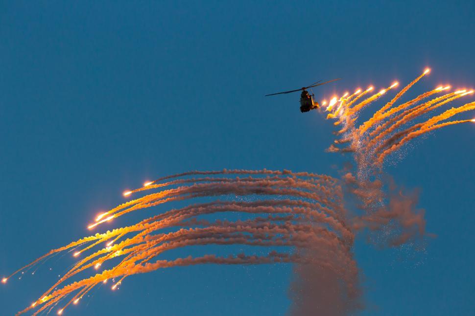 Free Image of A helicopter flying in the sky with fire trails 