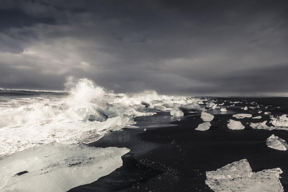 Free Image of Icebergs on a beach with waves crashing against them 