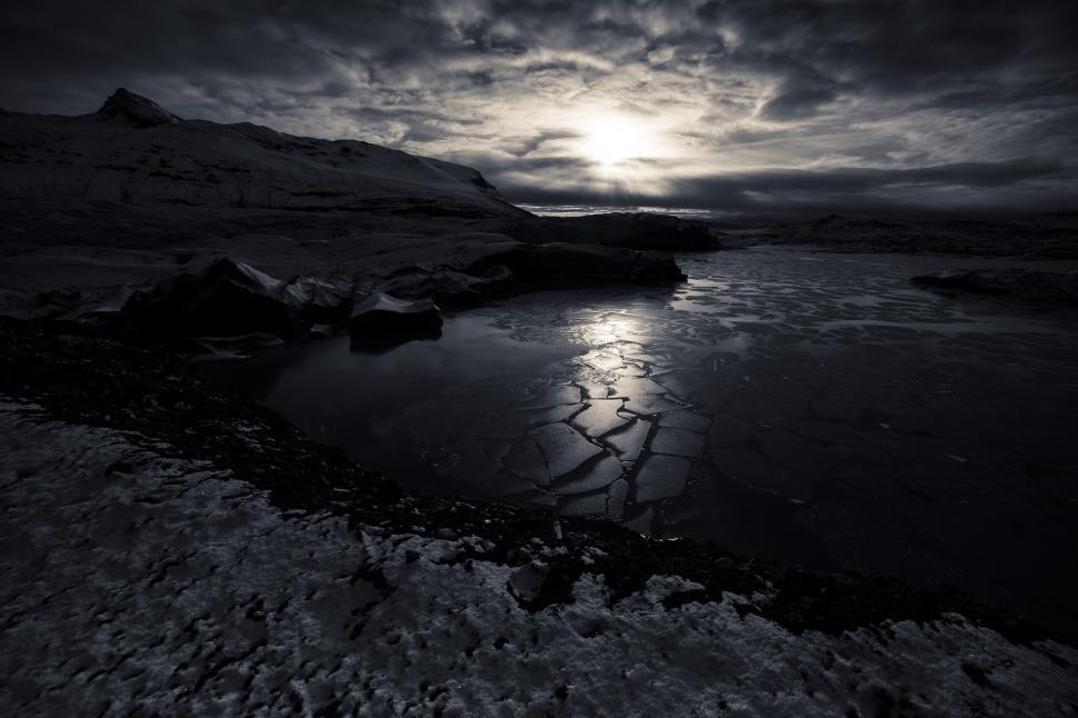 Free Image of A frozen lake with a snowy mountain and the sun shining through the clouds 