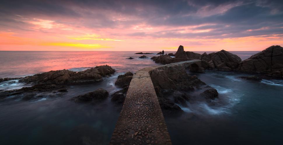Free Image of A stone walkway over rocks in the ocean 