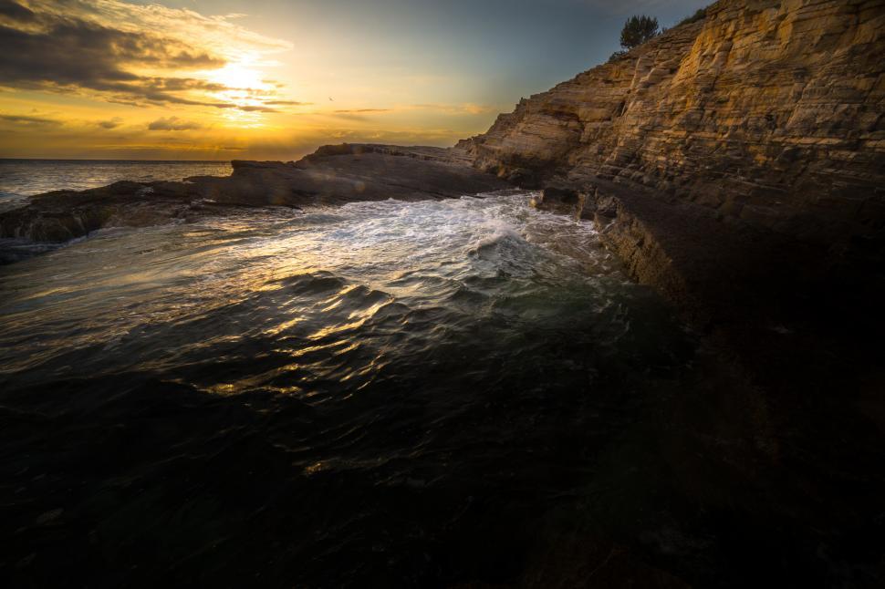 Free Image of A rocky beach with a body of water and a sunset 