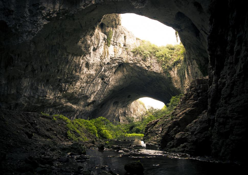 Free Image of A cave with a river and trees 