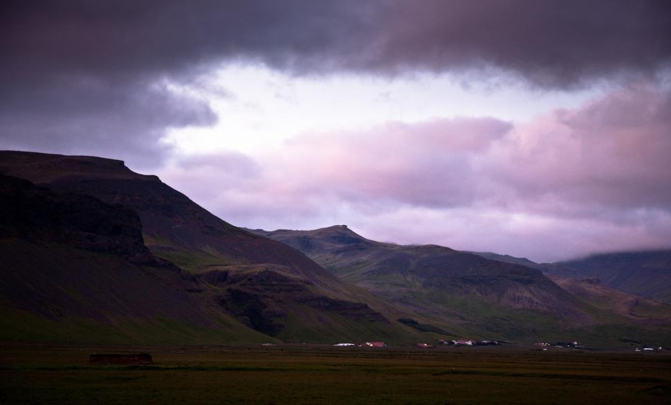 Free Image of A landscape of a green field with mountains and clouds 