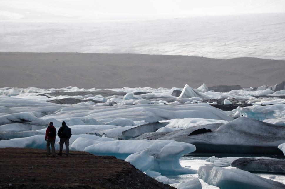 Free Image of Two people standing on a rocky shore looking at icebergs 
