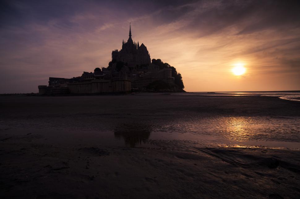 Free Image of A castle on a hill with a sunset in the background with mont saint-michel in the background 
