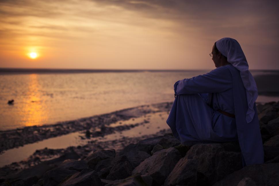 Free Image of A woman sitting on rocks looking at the sunset 